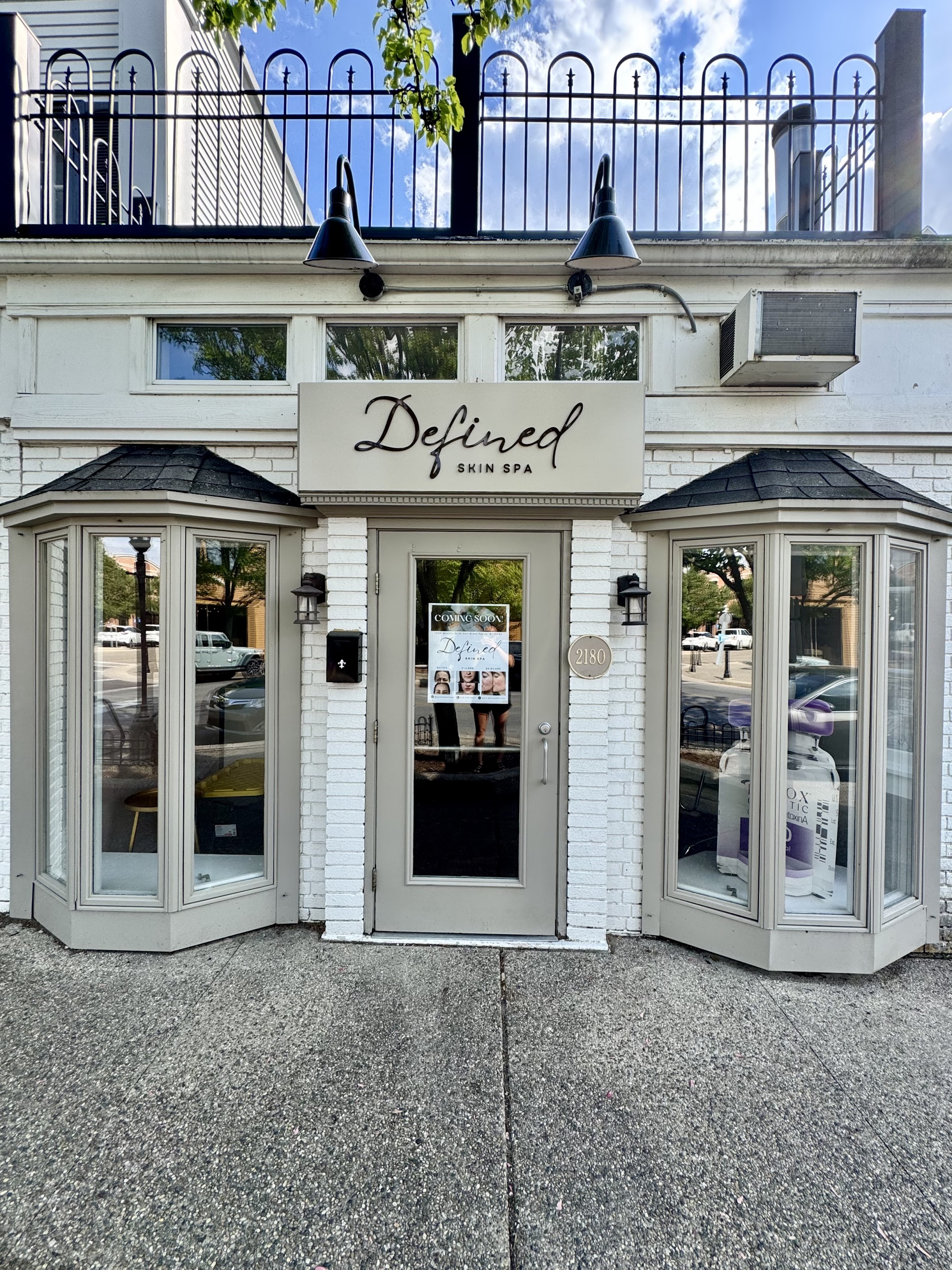 The Defined Skin Spa storefront in Gaslight Village — a white-brick bay-window facade with gaslight-style lamps and the cursive Defined sign